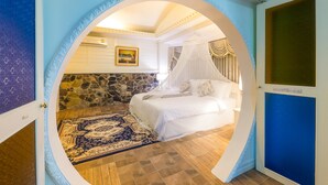 A bedroom with a stone wall, a bed with white bedding, a blue and gold patterned rug, and a painting on the wall. - Silamanee Resort and Spa Hotel (Mae Sai)