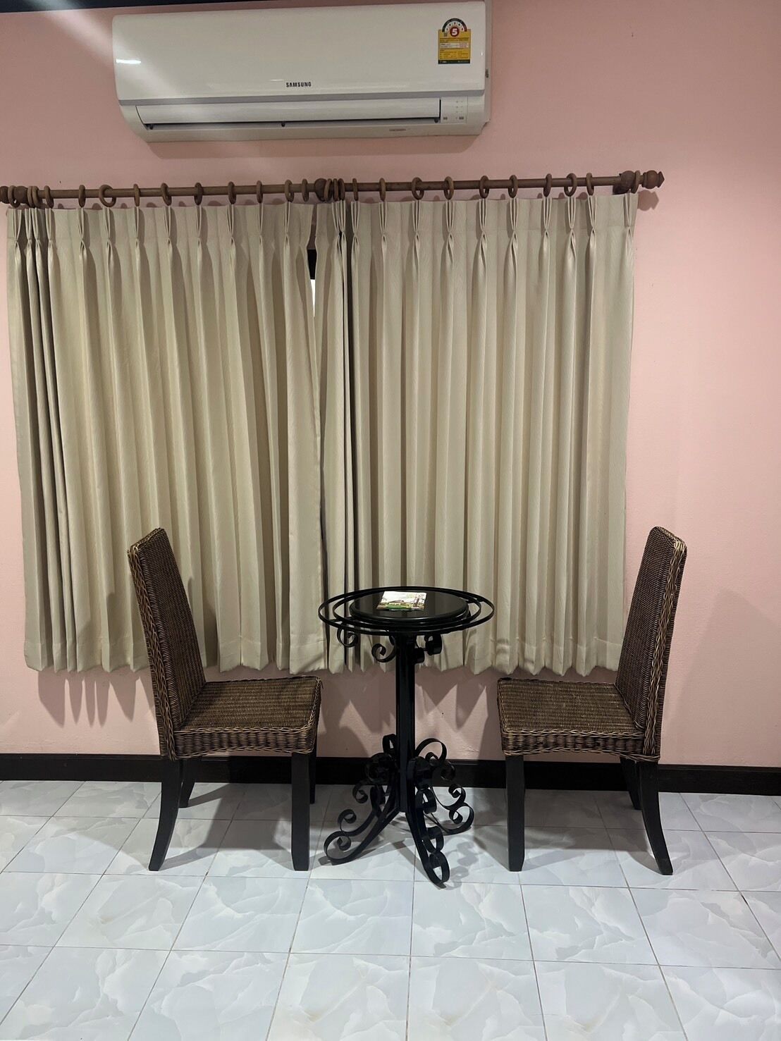 A room with a table and two chairs, an air conditioner, and a curtain.