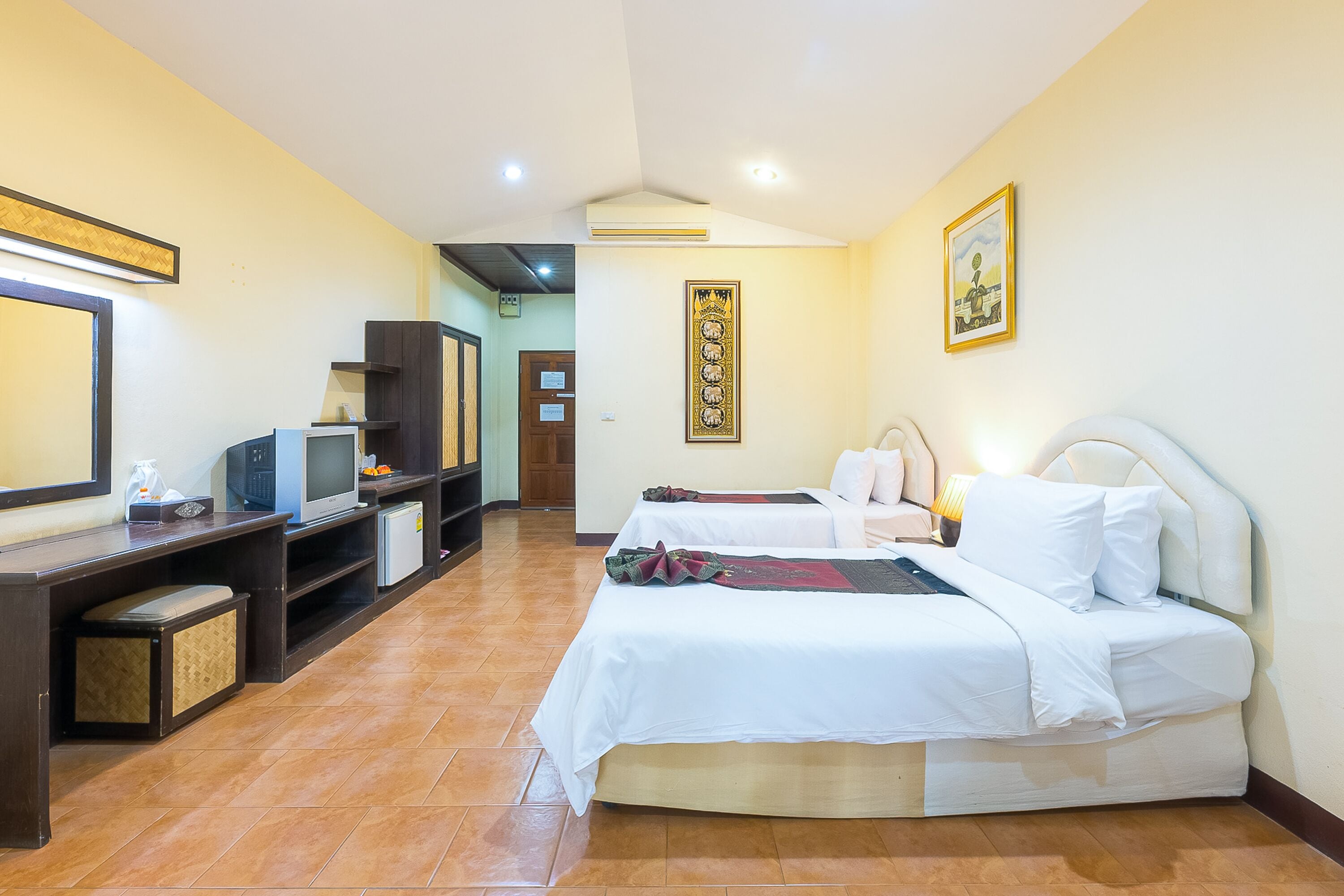 Una habitación de hotel con dos camas, un escritorio con computadora, televisor y minibar.