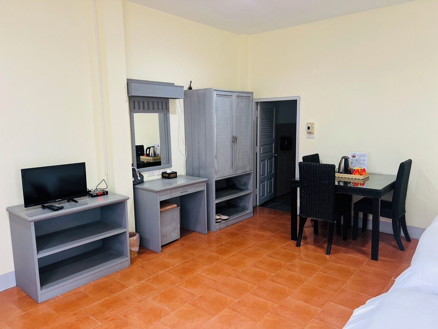 Une chambre d’hôtel de taille réduite, équipée d’une télévision, d’un bureau avec une chaise, d’une armoire et d’une petite table à manger avec des chaises.