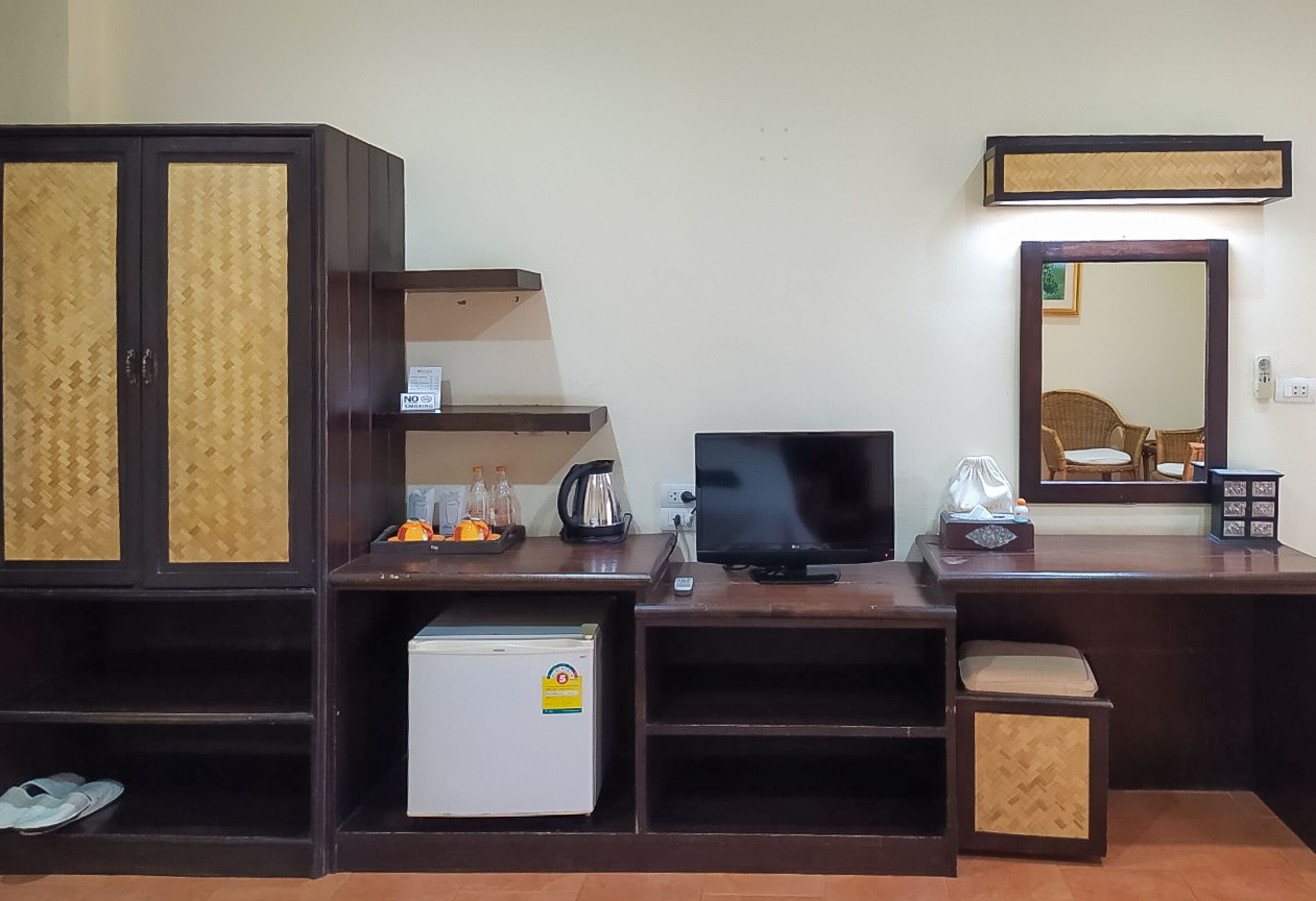 A compact room with a TV, a small refrigerator, a cabinet, a mirror, and a shelf with toiletries.