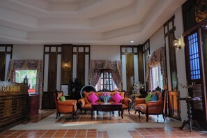 A spacious lobby with a reception desk, leather armchairs, a coffee table, and large windows with curtains.
