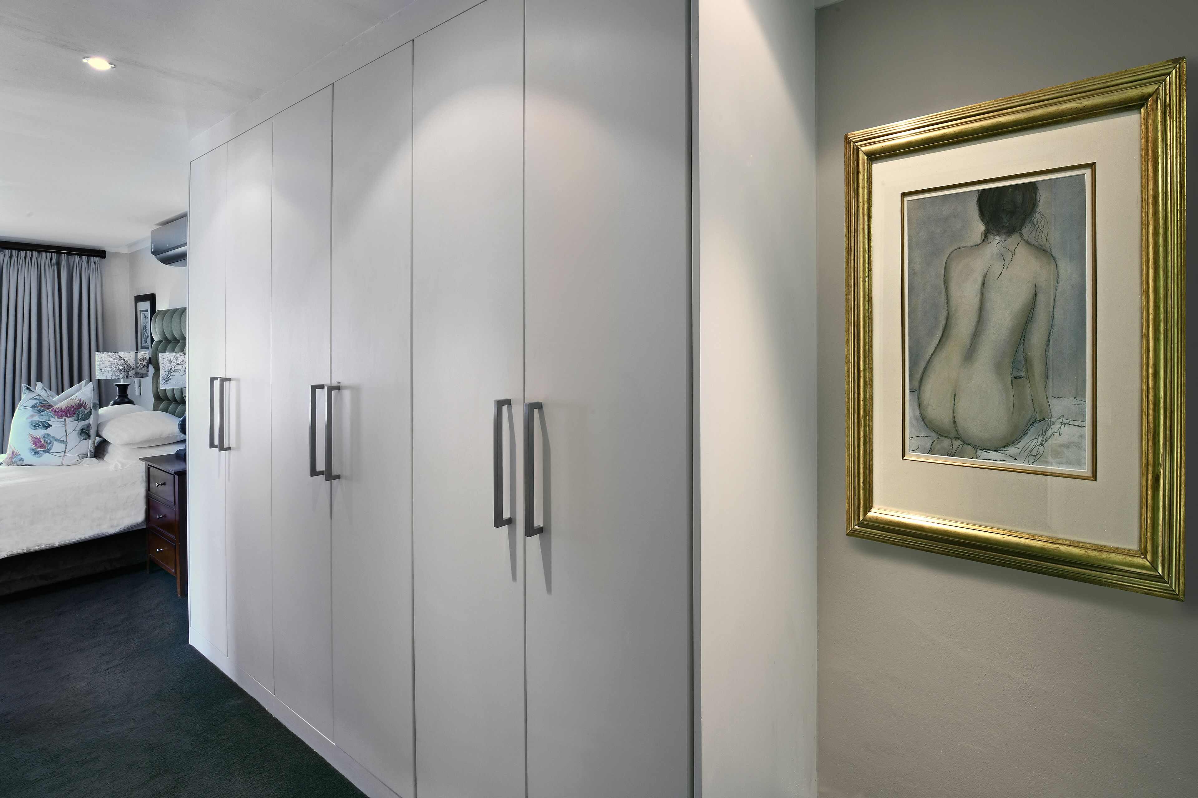 A hotel room with a bed, a wardrobe, and a framed artwork on the wall.