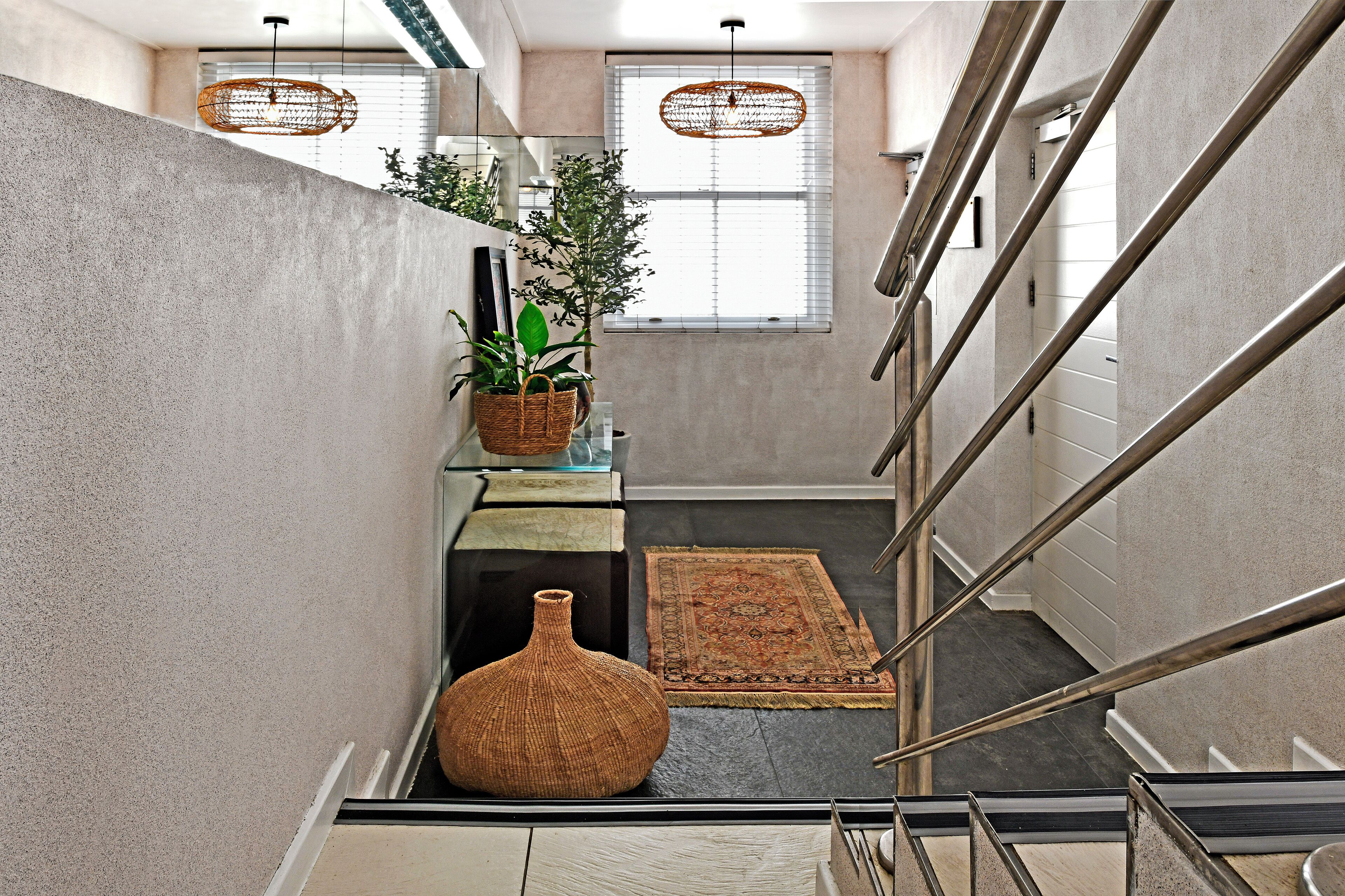 A modern staircase with metal railings, a concrete wall, a wicker basket with a plant, a woven basket, and a large vase.