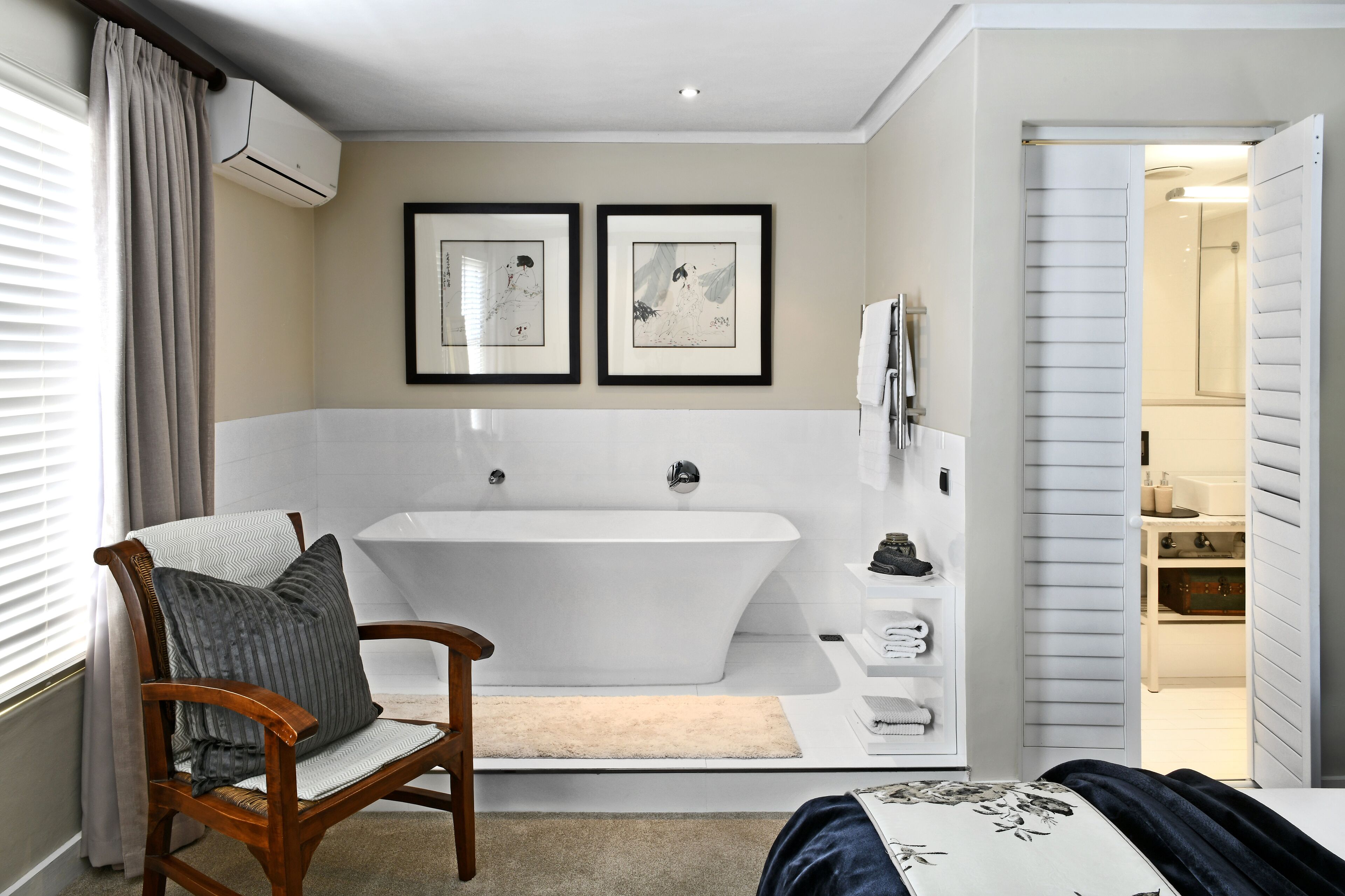 A modern bathroom with a freestanding bathtub, a wooden chair, and two framed artworks on the wall.