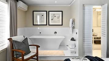 A modern bathroom with a freestanding bathtub, a wooden chair, and two framed artworks on the wall.