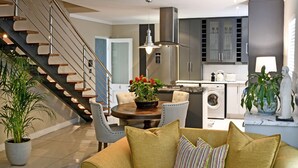 A modern kitchen with stainless steel appliances, a dining area with a round table and chairs, and a staircase with a wooden finish. - Le Petit Bijou Boutique Aparthotel (Franschhoek)