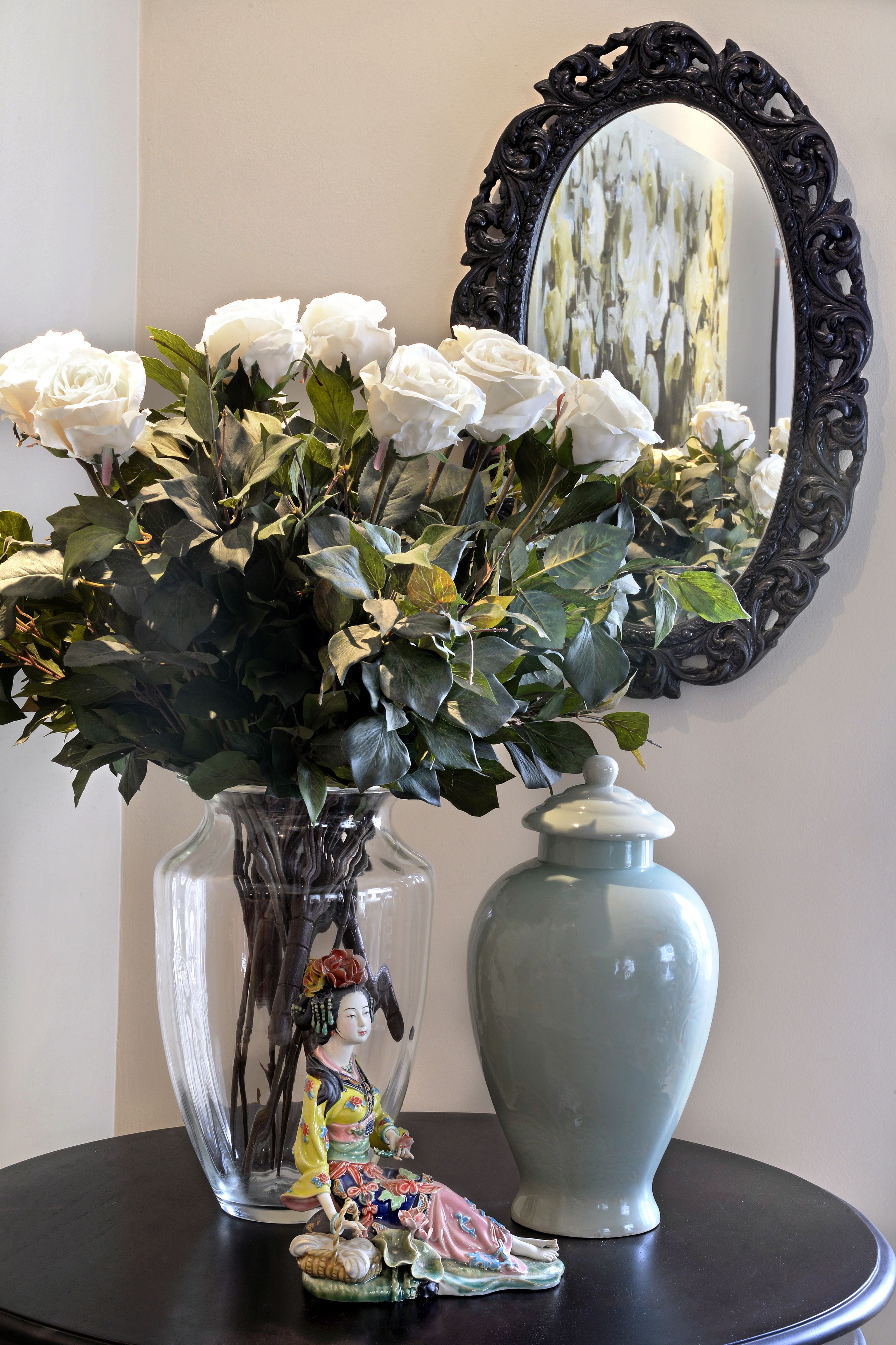 Un jarrón con flores blancas y una figurita sobre una mesa.