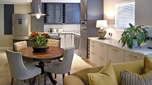A modern kitchen with dark cabinets, a dining table with chairs, and a potted plant on the counter. - Le Petit Bijou Boutique Aparthotel (Franschhoek)