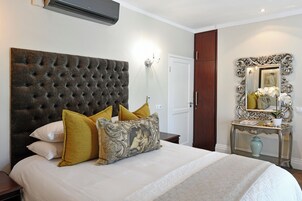 Cama bem arrumada com cabeceira acolchoada, mesa de cabeceira com um vaso e espelho com moldura elaborada.