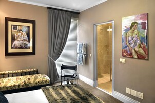 Una habitación de hotel con cama, un banco, zona de ducha y dos cuadros en las paredes.