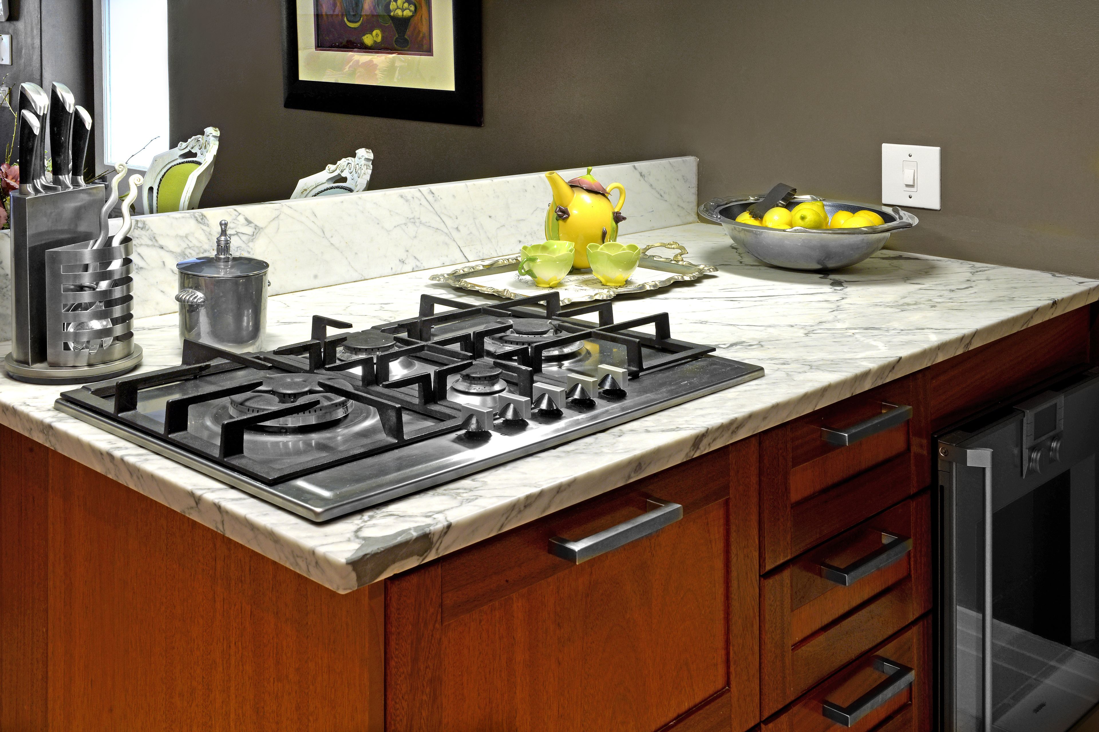 A kitchen with a gas stove, wooden cabinets, a marble countertop, and a bowl of lemons.