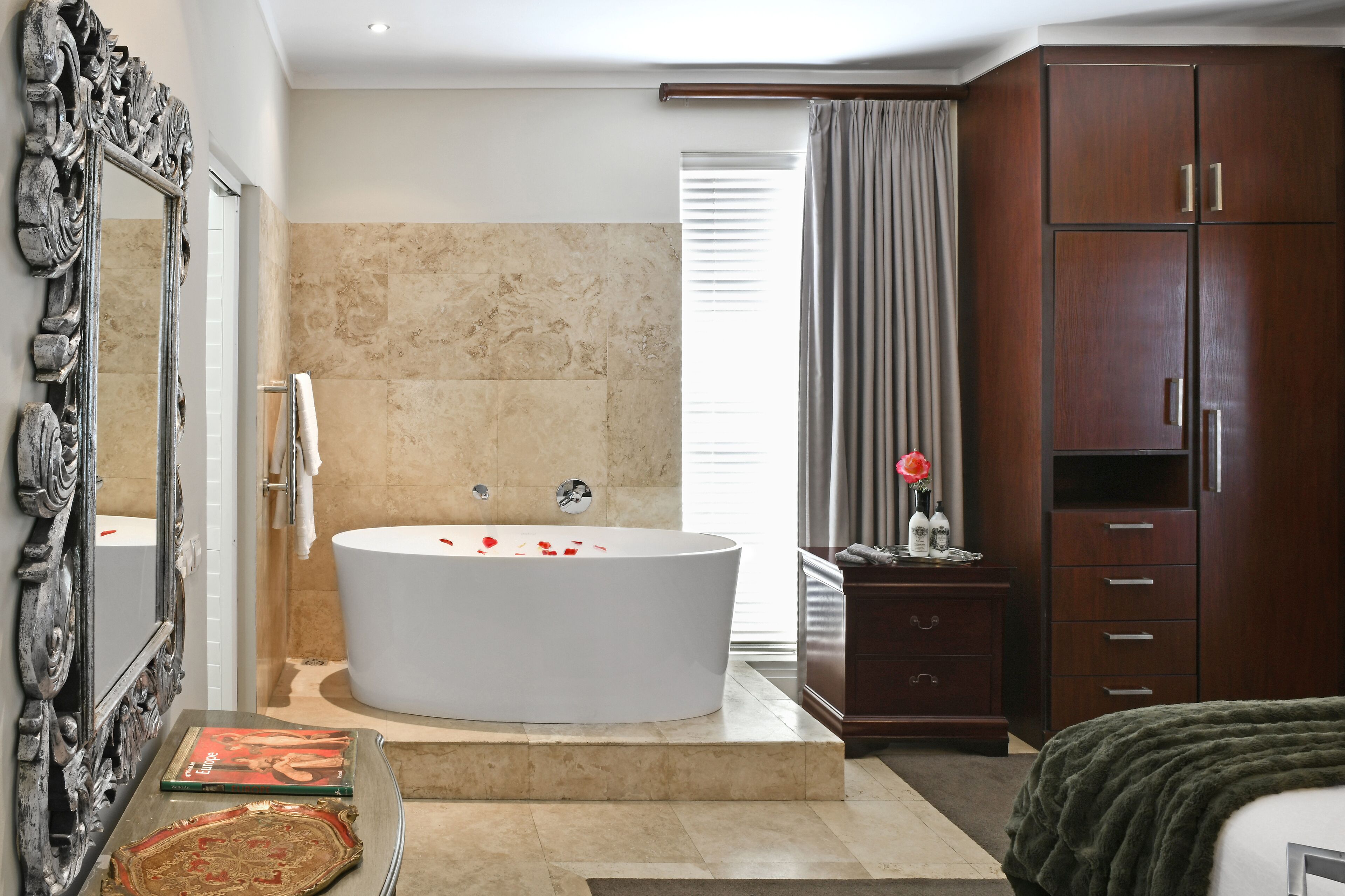 A modern bathroom with a freestanding bathtub, a large mirror, and a wooden wardrobe.