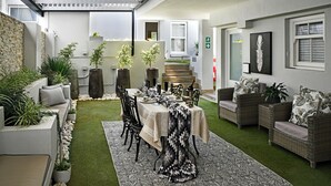 A patio with a dining table set for four, surrounded by wicker furniture and potted plants. - Le Petit Bijou Boutique Aparthotel (Franschhoek)