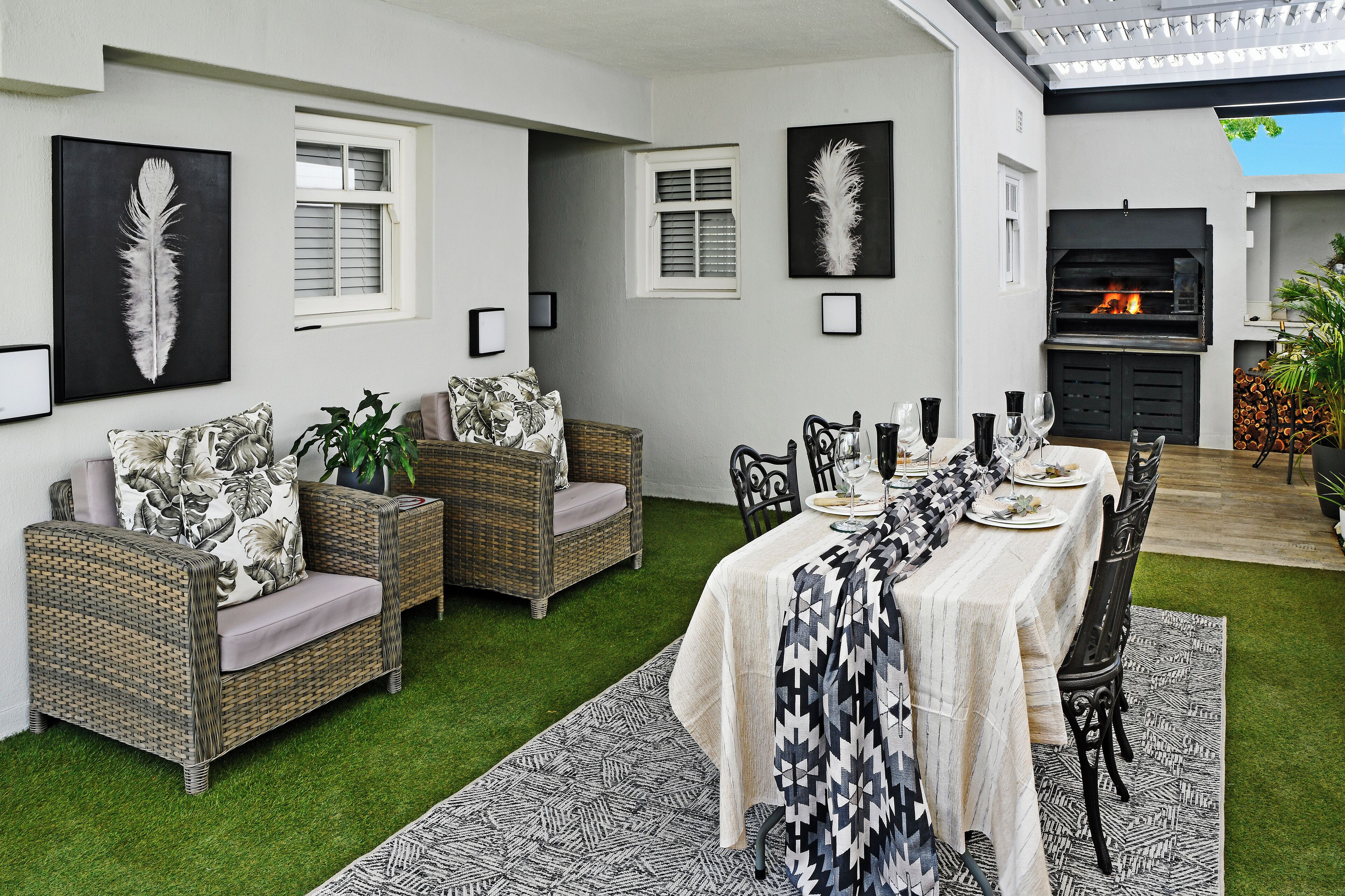 Comedor con una mesa larga dispuesta para cuatro personas, rodeado de muebles de mimbre y un tapete estampado.