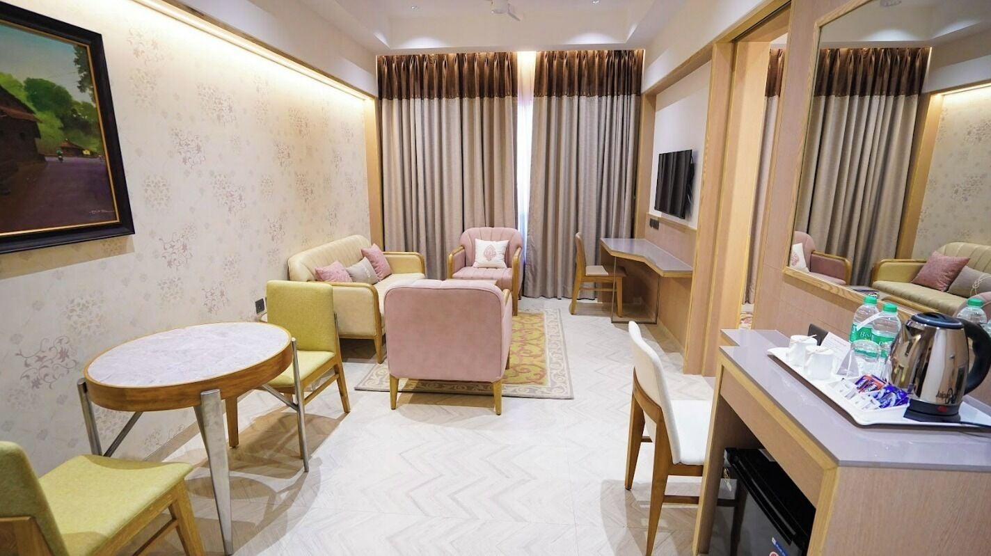 A hotel room with a round table, two armchairs, a sofa, a TV, and a minibar.
