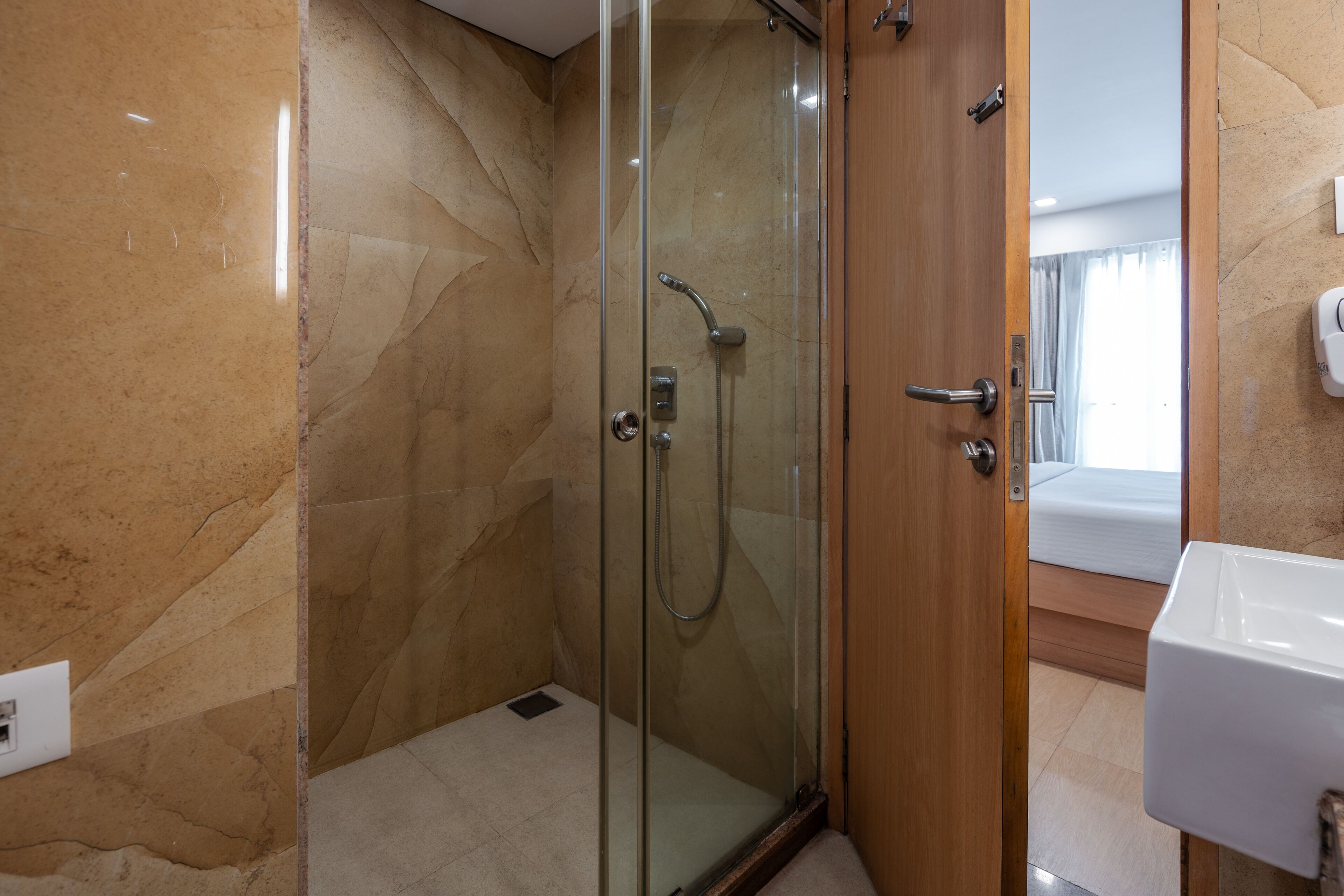 A modern bathroom with a glass-enclosed shower, a wooden door, and a white sink.