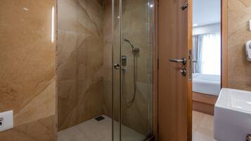 A modern bathroom with a glass-enclosed shower, a wooden door, and a white sink.