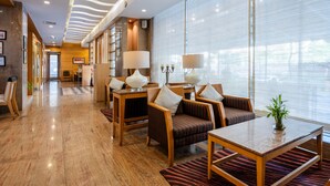 A hotel lobby with a wooden floor, seating area with tables and chairs, and large windows with blinds. - GCC Northside Hotel (Mumbai)