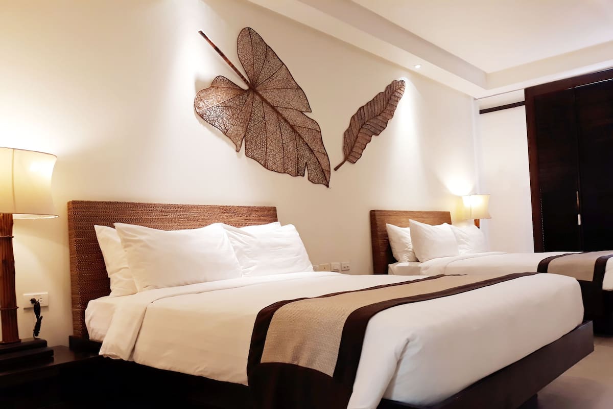Une chambre d’hôtel avec deux lits, chacun doté de draps blancs et d’une tête de lit sombre. Des lampes murales sont fixées de chaque côté des lits.