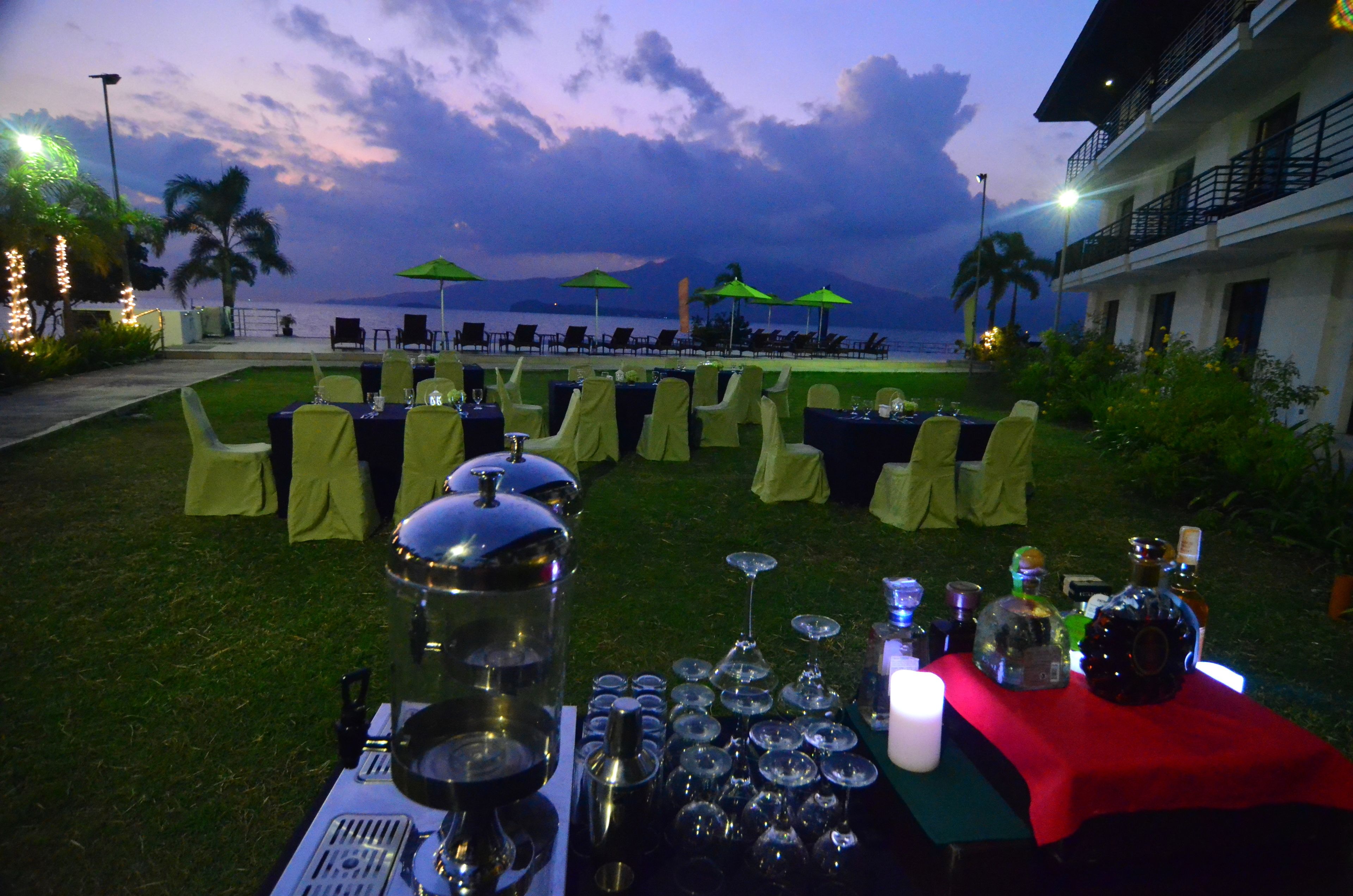 An outdoor dining area with tables set for a meal, overlooking a body of water and palm trees.