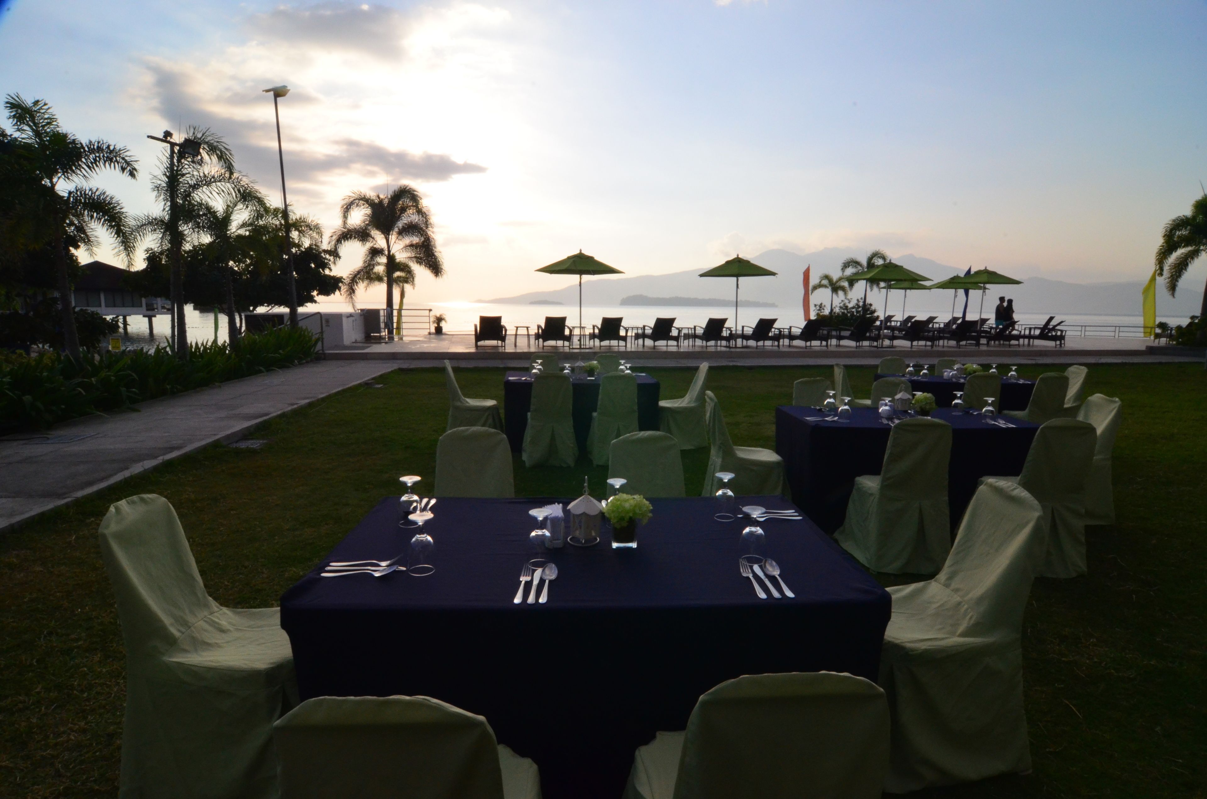 An outdoor dining area with tables set for guests, overlooking a body of water and mountains.