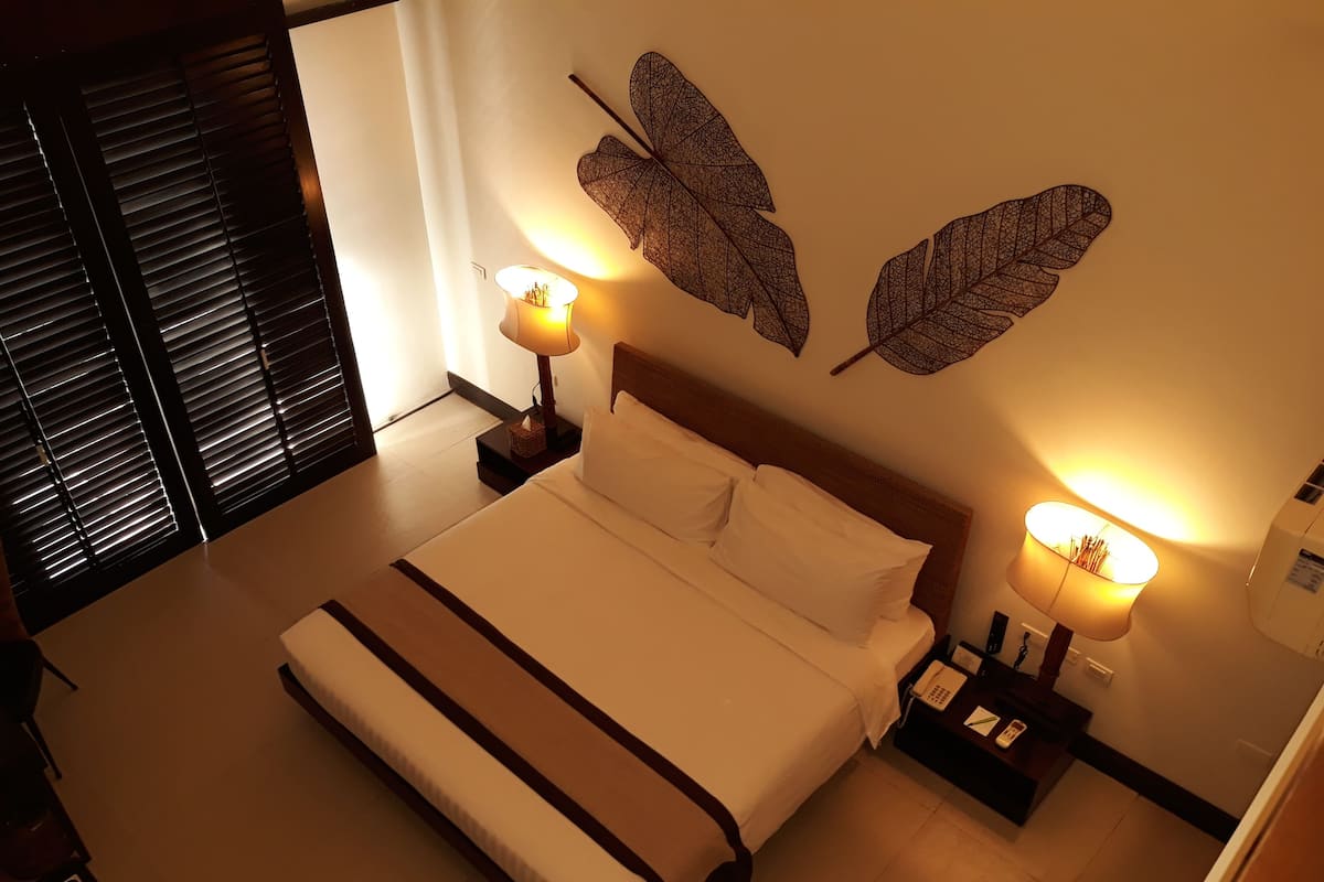 Un lit bien fait, avec une tête de lit en bois, deux lampes fixées au mur et des motifs décoratifs en forme de feuilles sur le mur.