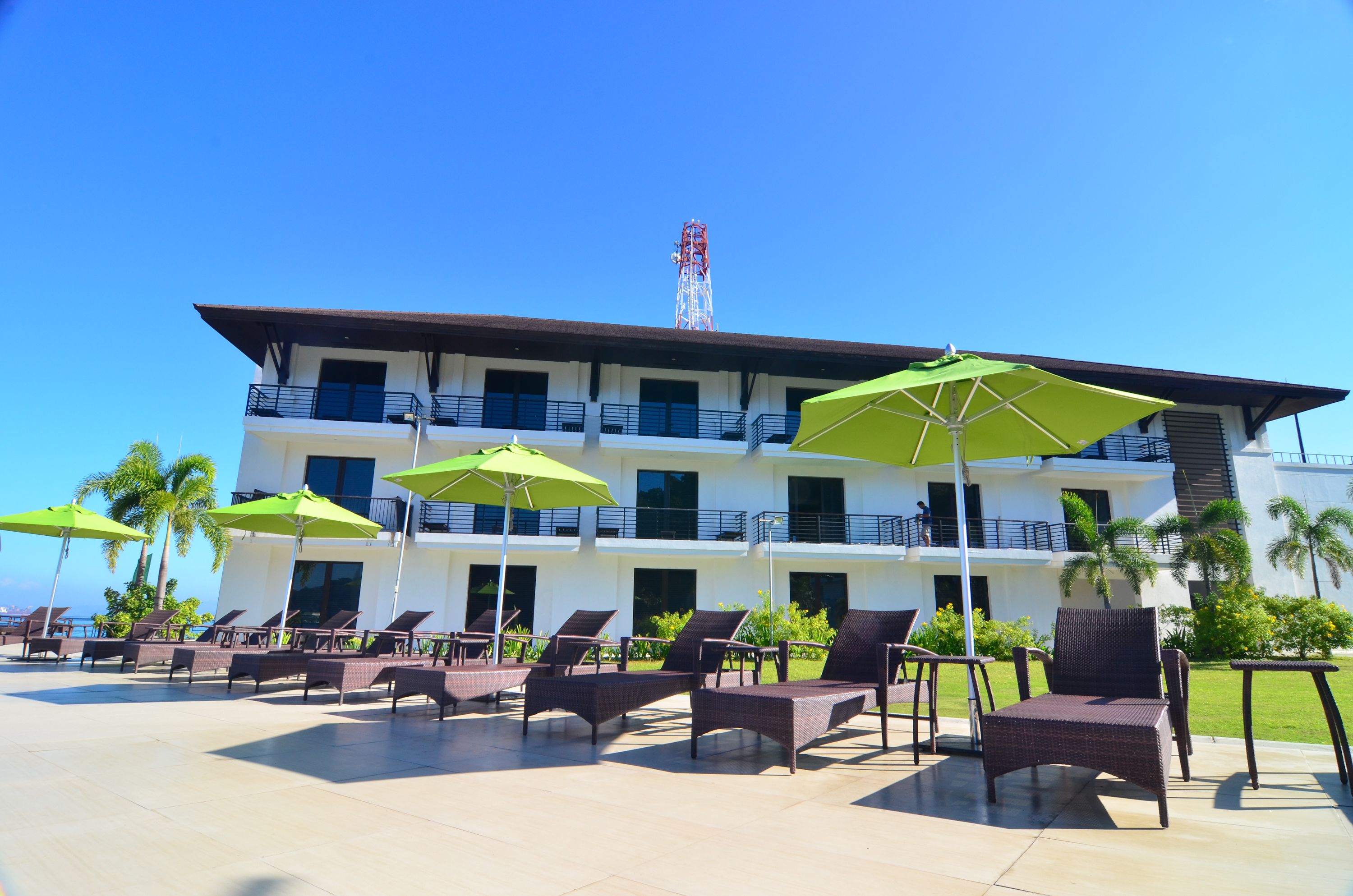 A hotel with multiple floors, outdoor seating with umbrellas, and a clear view of the sky.