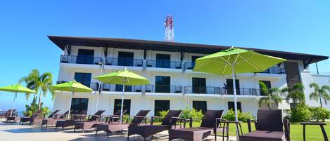 A hotel with multiple floors, outdoor seating with umbrellas, and a clear view of the sky.