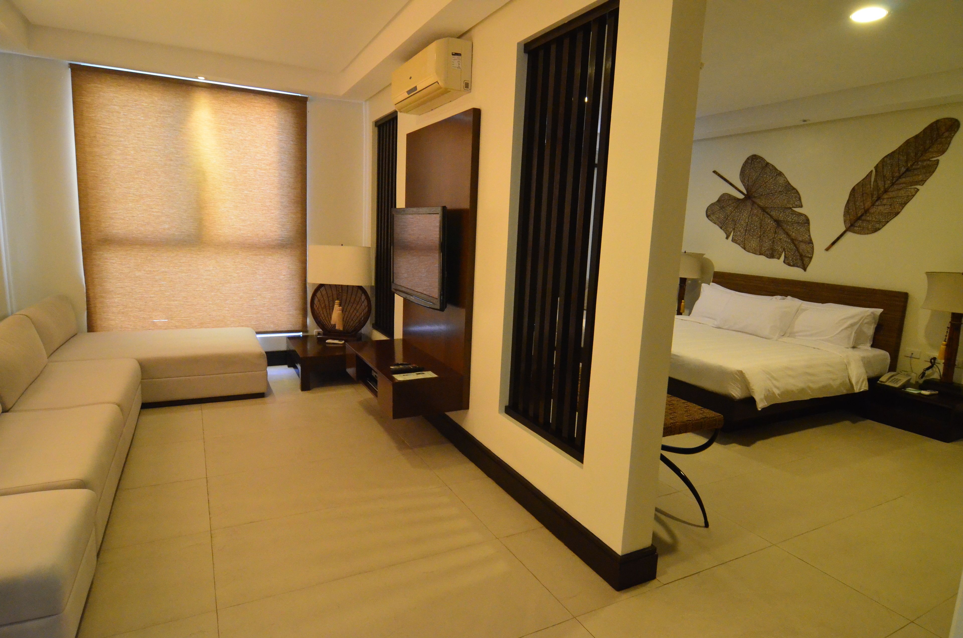 Habitación de hotel con sofá, cama, televisión y pared decorada con motivos vegetales.