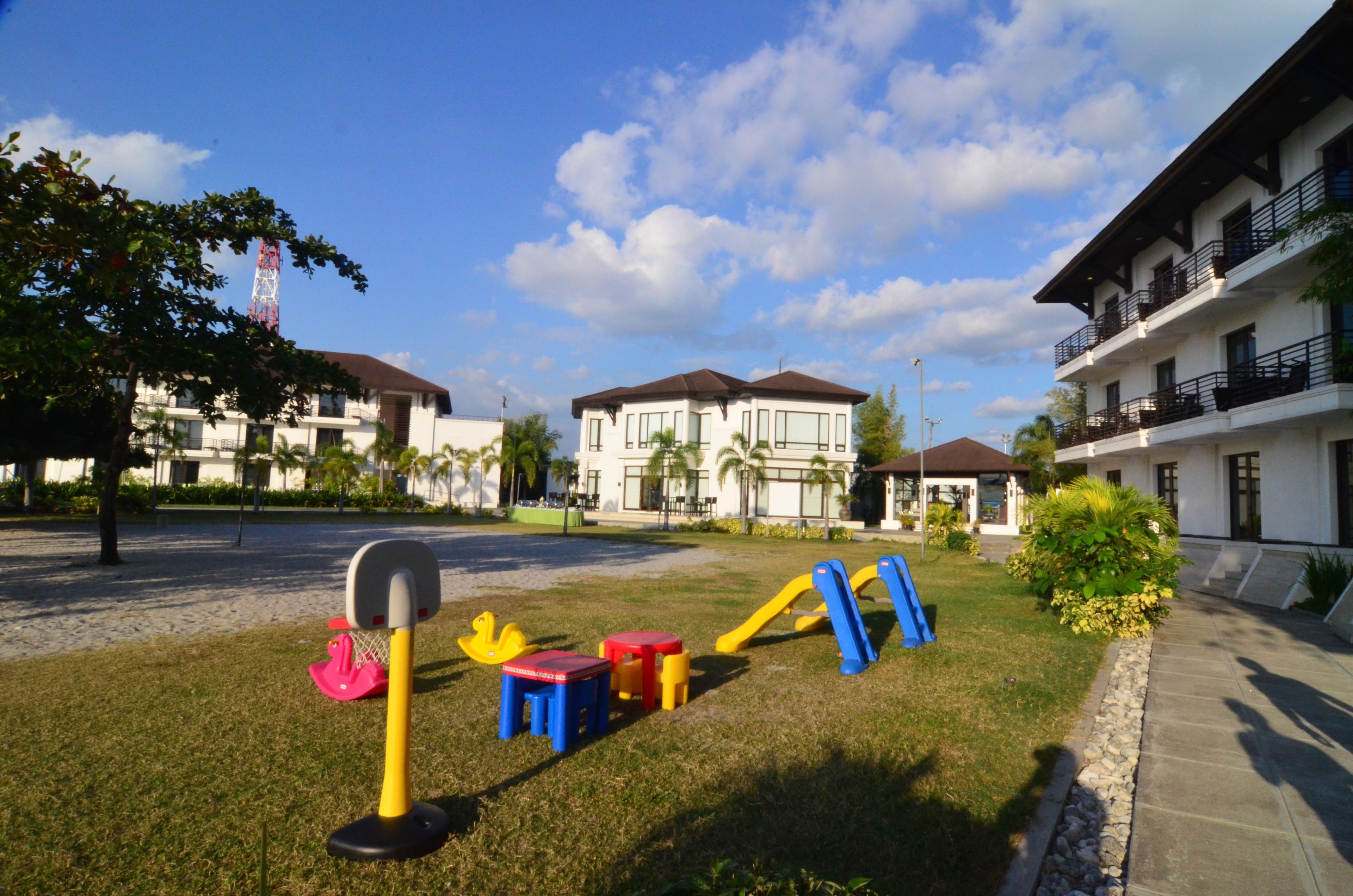 A playground with colorful equipment, a building with balconies, and a clear sky.