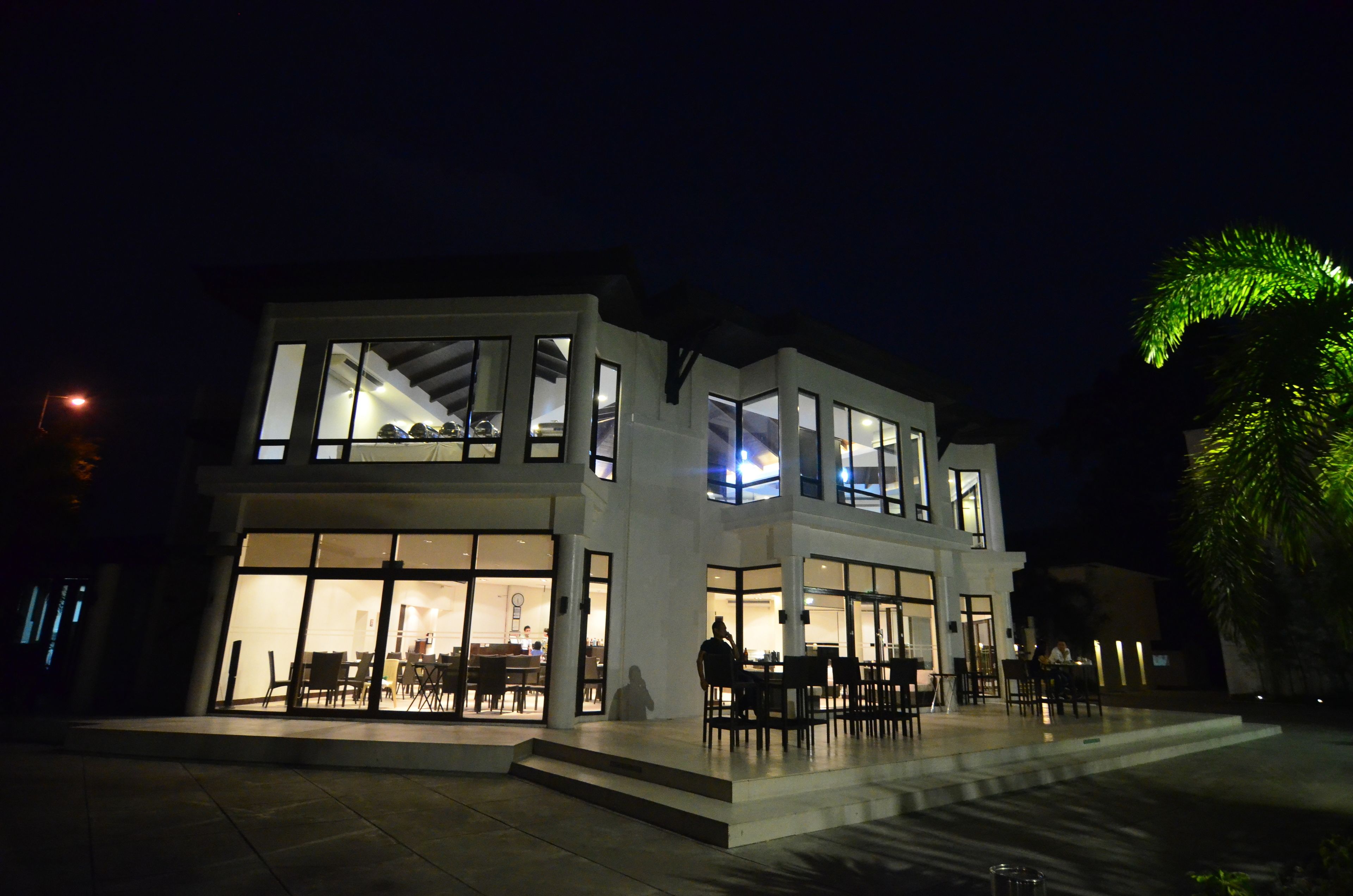 Un moderno edificio de dos pisos con amplias ventanas y un patio con mobiliario exterior.