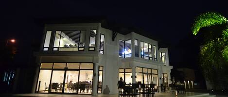 Un moderno edificio de dos pisos con amplias ventanas y un patio con mobiliario exterior.