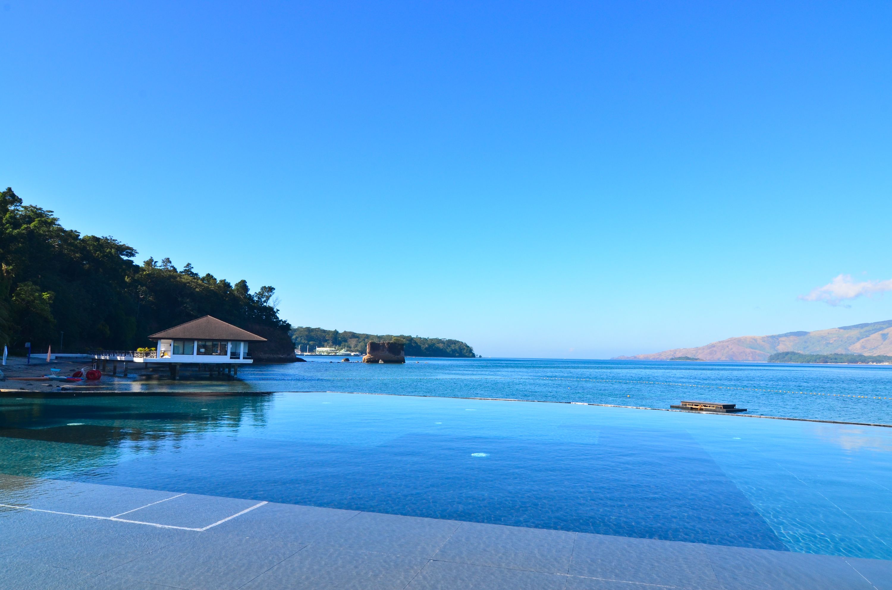 Ein Pool im Unendlickkeits-Design mit klarem, blauem Wasser, ein kleines Gebäude und eine anlegbare Plattform, die ins Wasser führt.