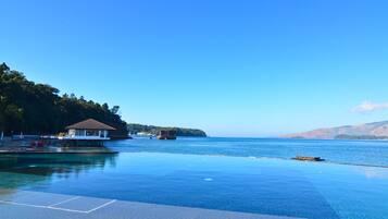 Ein Pool im Unendlickkeits-Design mit klarem, blauem Wasser, ein kleines Gebäude und eine anlegbare Plattform, die ins Wasser führt.