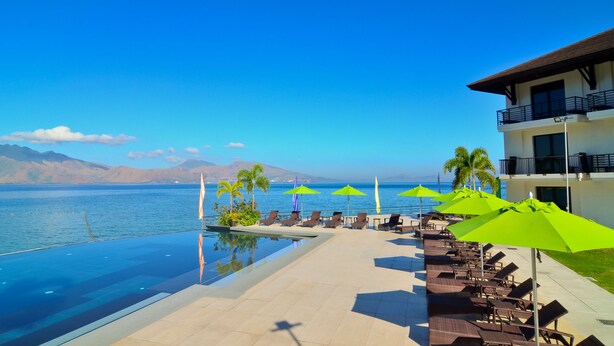 An infinity pool with a view of the sea and mountains, lounge chairs, and umbrellas. - Hotel Kamana Sanctuary Resort and Spa (Morong)