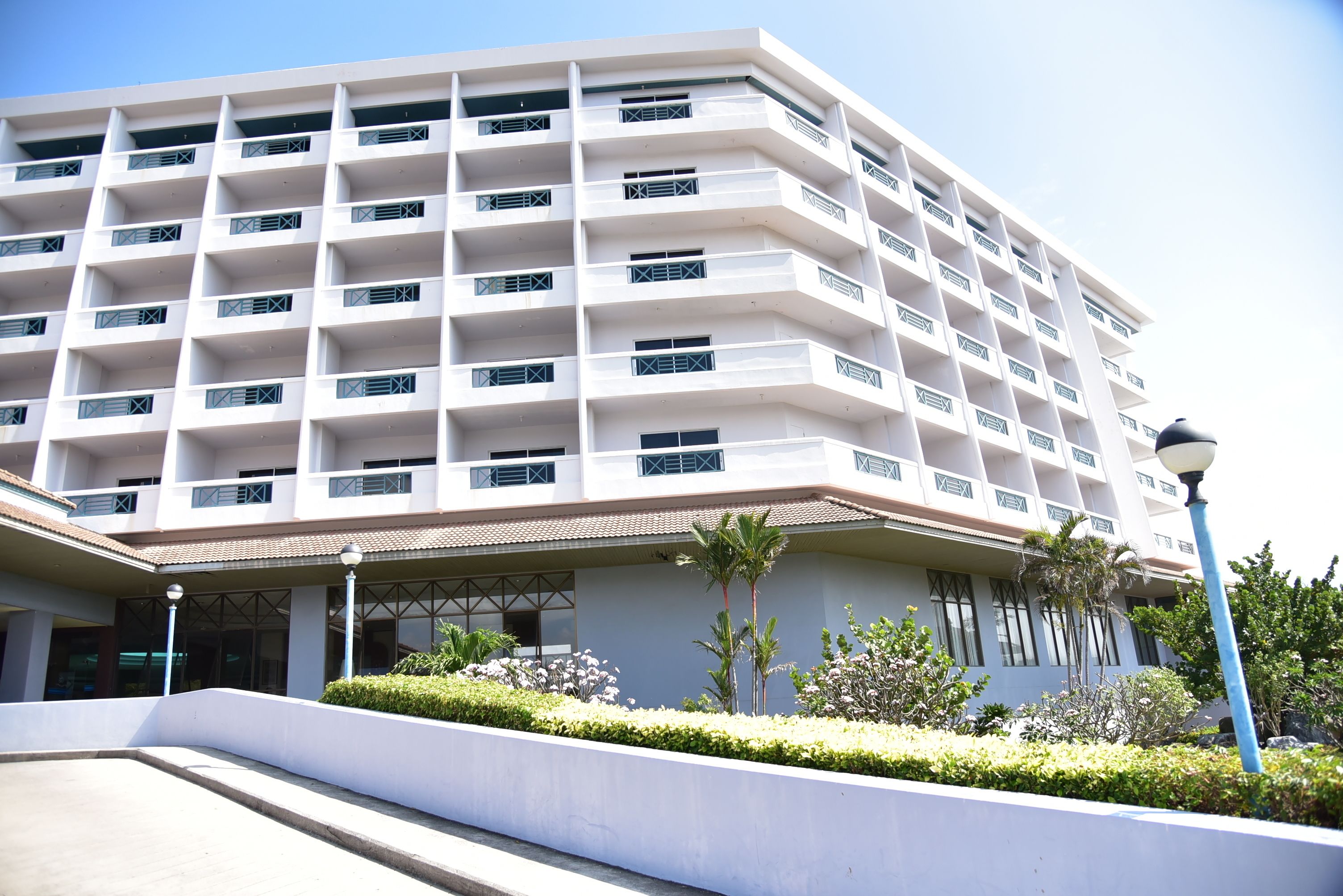 A multi-story hotel with a modern design, featuring balconies on each floor and a landscaped entrance area.