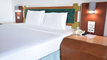 A hotel room with a large bed, a wooden headboard, a bedside telephone, and a wall-mounted light fixture.