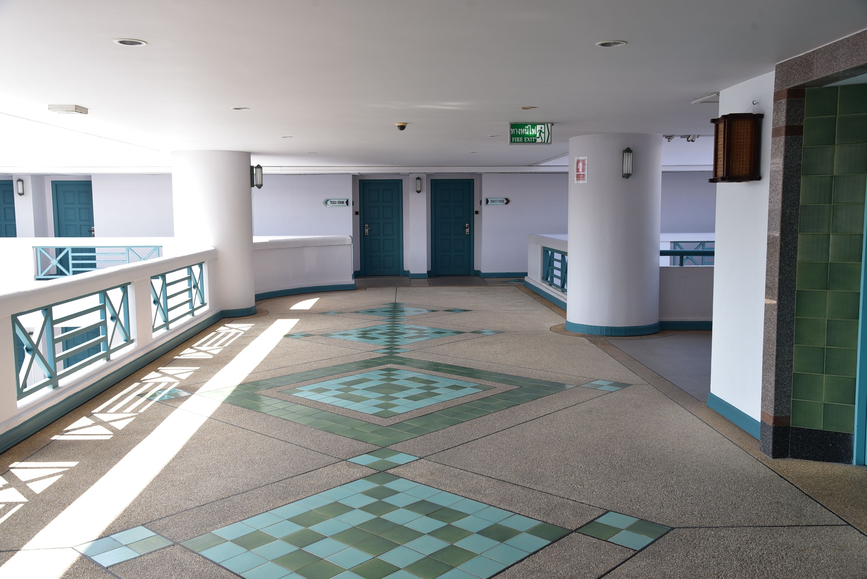 A corridor with a geometric patterned floor, teal doors, and a fire exit sign.