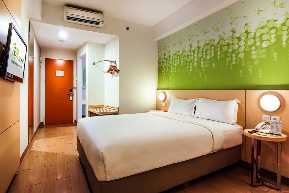 Habitación de hotel con cama, mesita de noche con teléfono, aire acondicionado de pared y pared verde con un diseño circular.