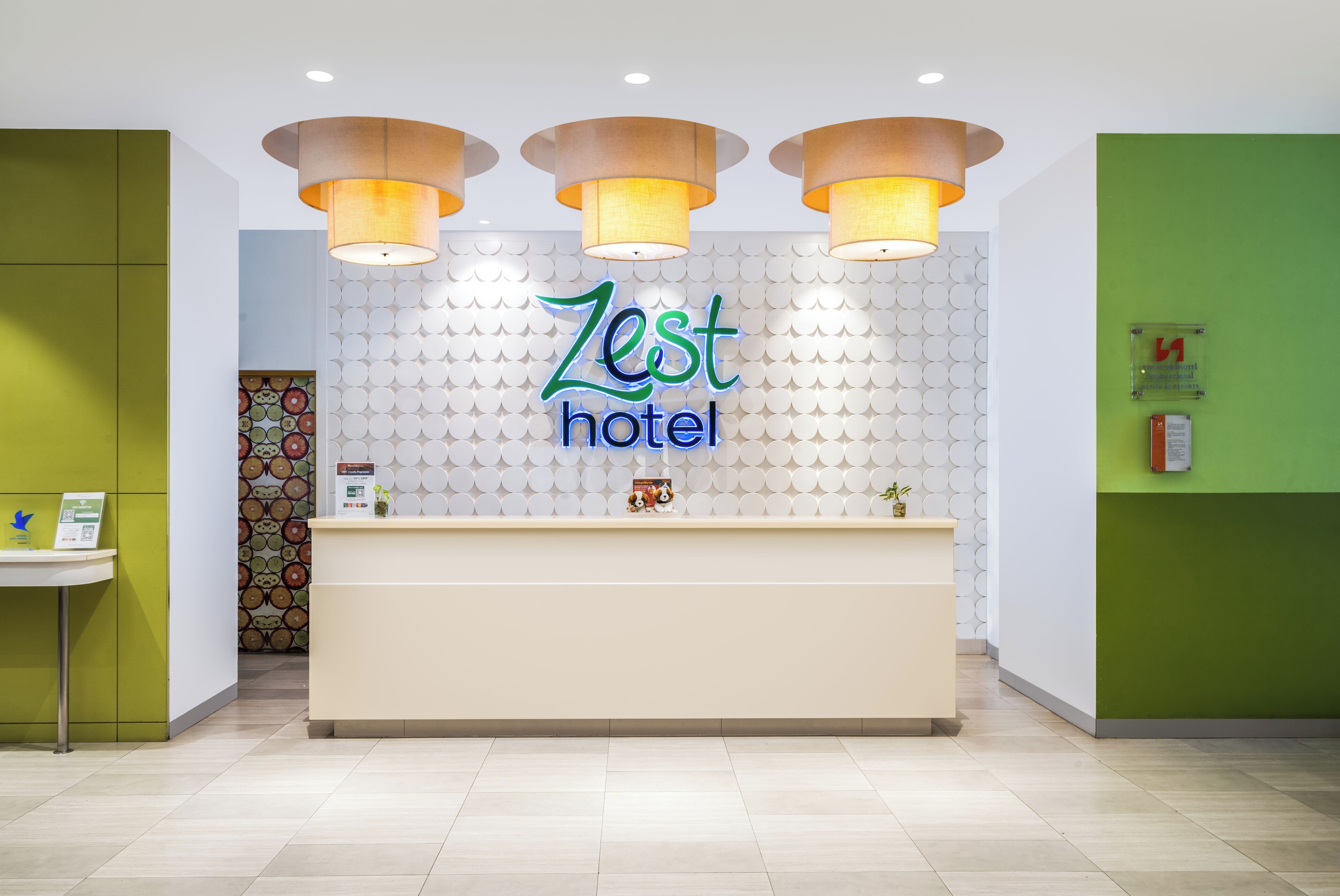 Ein Empfangsschalter mit einem Schild 'Zest Hotel', einer grünen Wand und einer Wand mit Muster im Hintergrund.