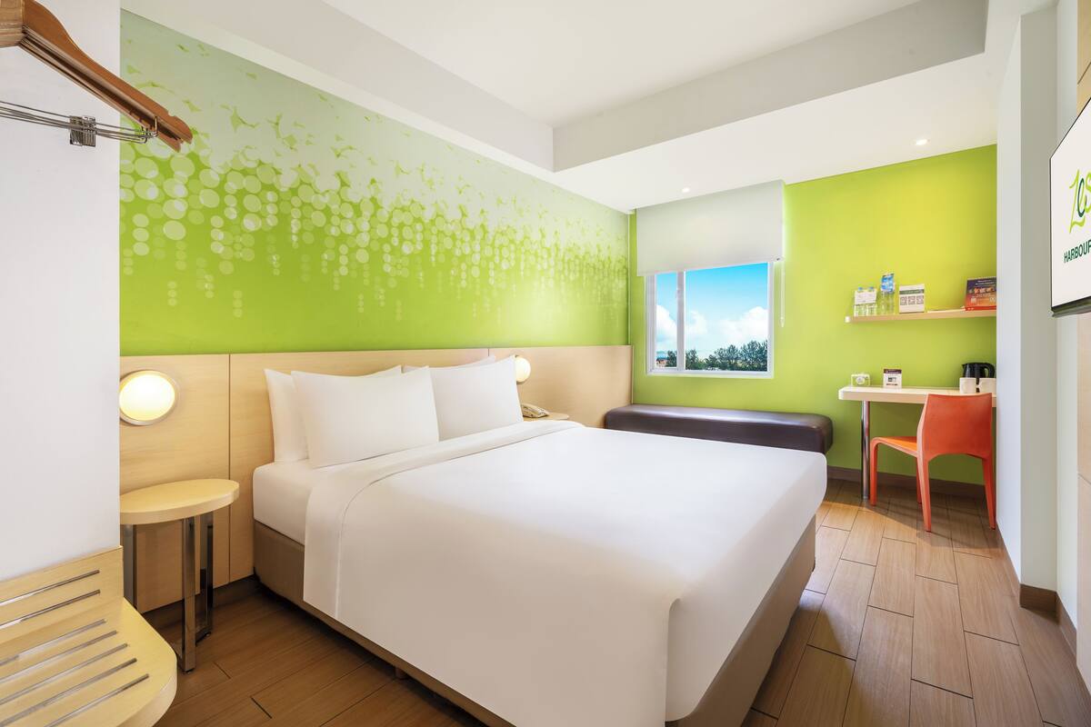 Ein Hotelzimmer mit einem großen Bett, einem Schreibtisch mit Stuhl, einem kleinen Tisch und einem Fenster mit Blick.