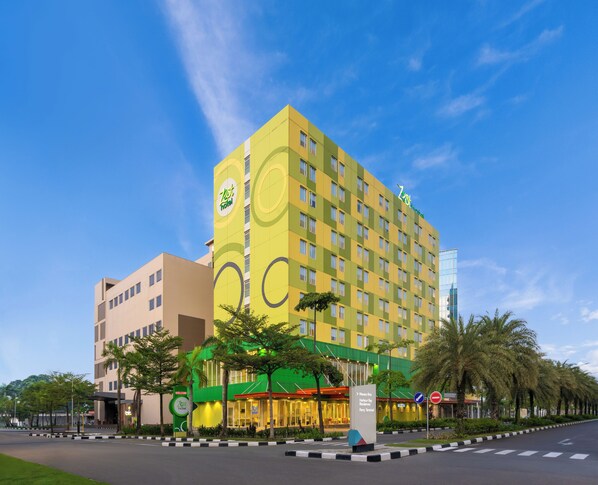A hotel with a modern design, featuring a prominent logo on the facade, a well-lit entrance, and a clear view of the surrounding area including a road and palm trees. - Zest Harbour Bay Batam by Swiss-Belhotel International (Batam)
