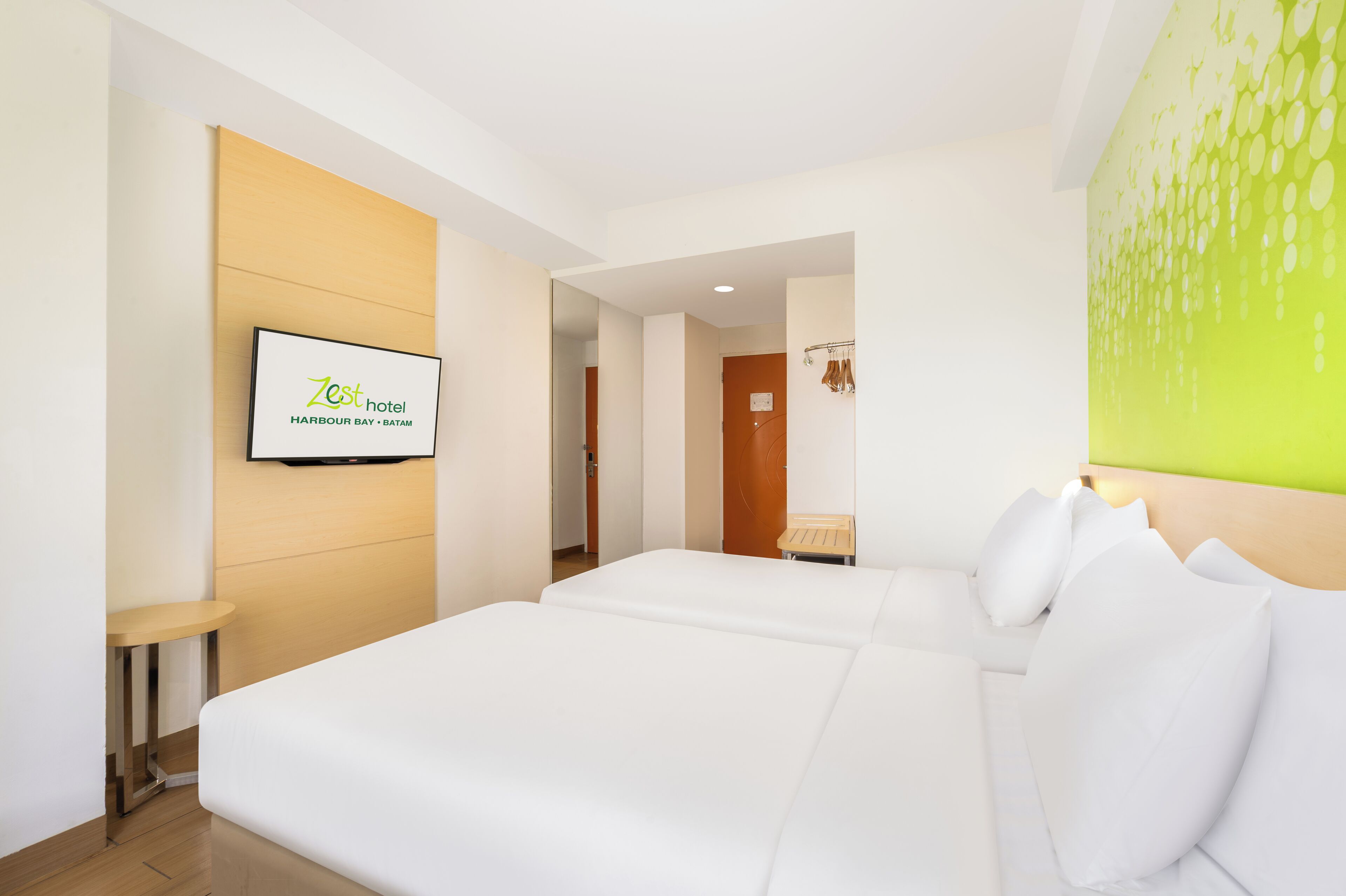 A hotel room with a bed, a TV mounted on the wall, and a wooden headboard.