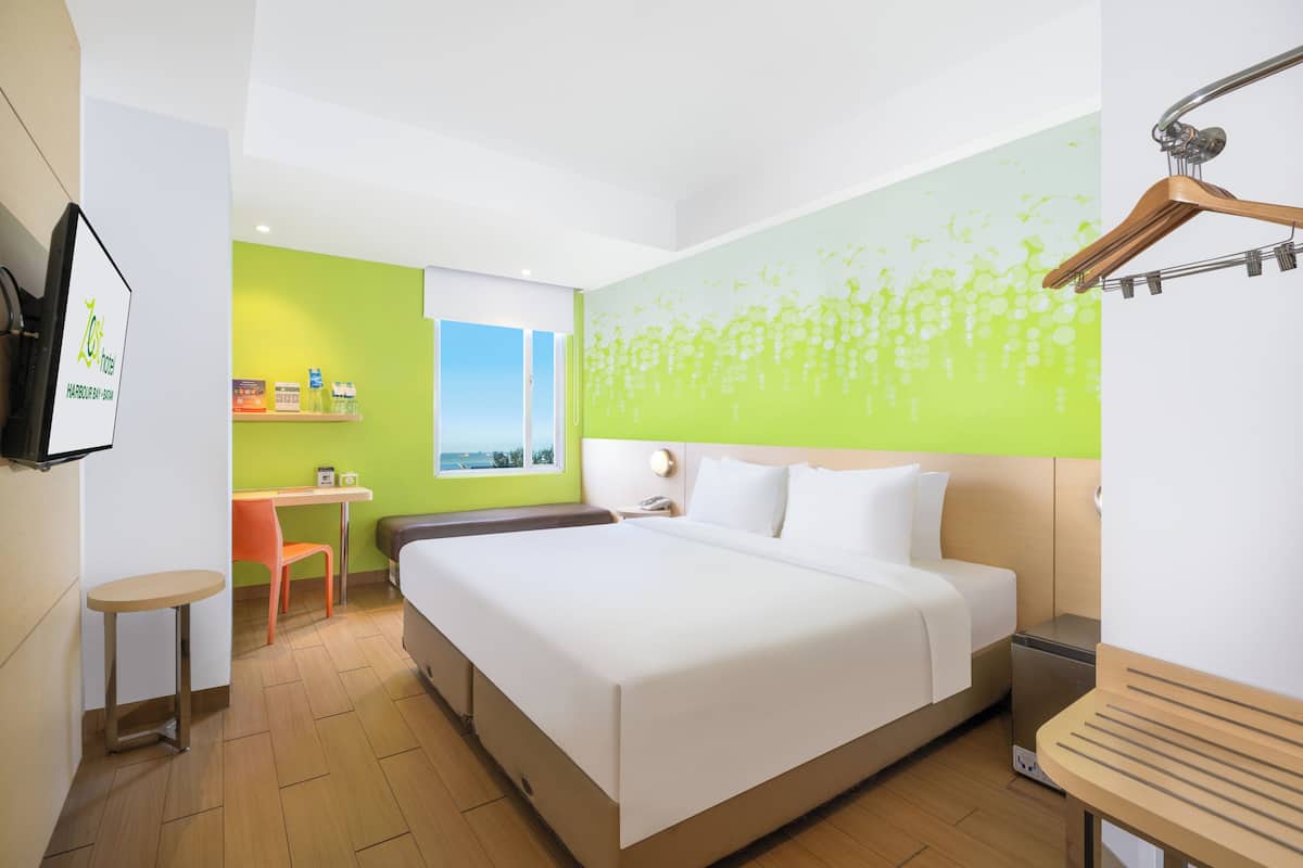 Ein Hotelzimmer mit einem großen Bett, einem Schreibtisch, einem Stuhl, einem kleinen Tisch und Blick ins Freie.