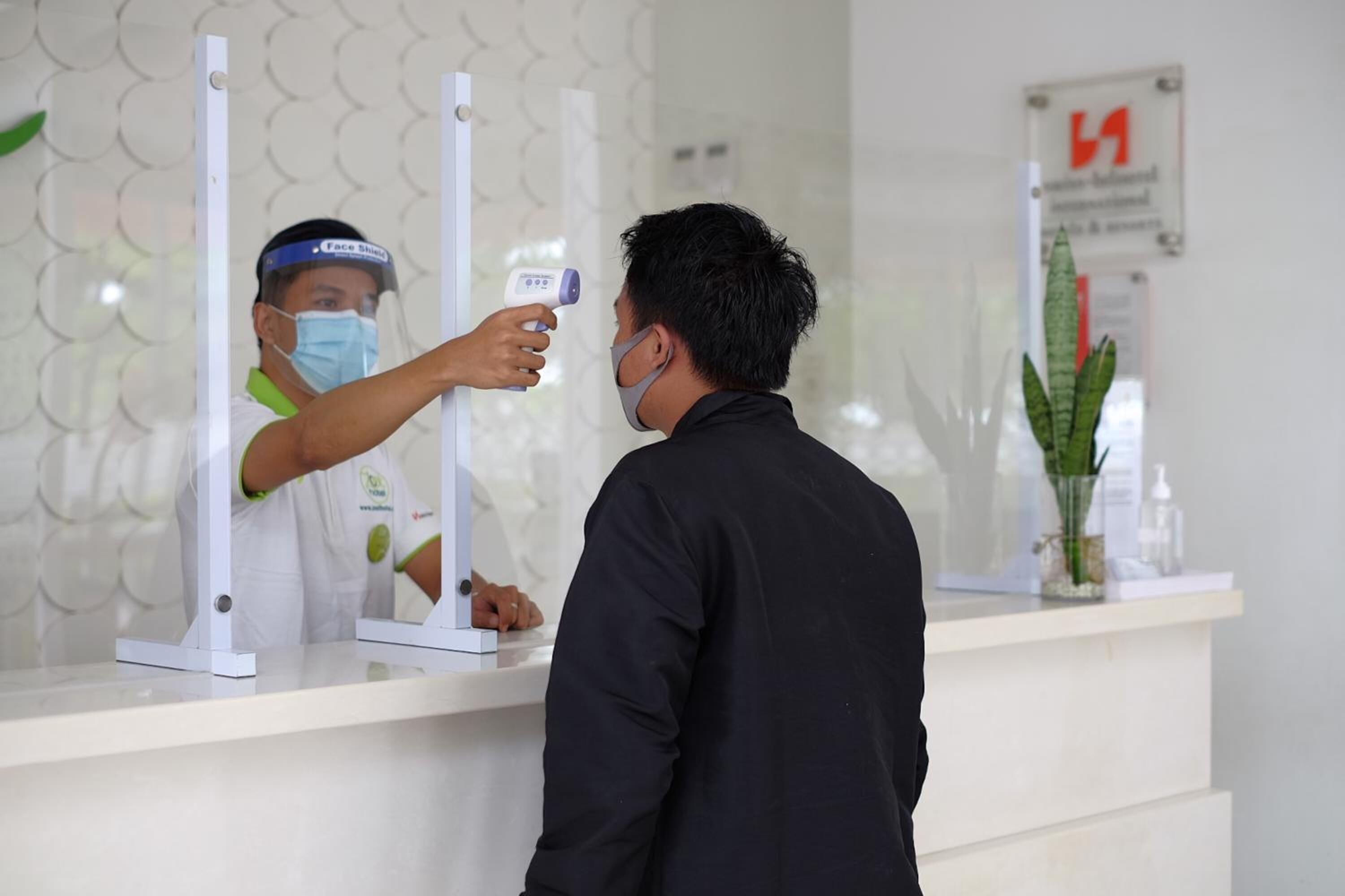 A person being screened with a thermal scanner at a reception desk.