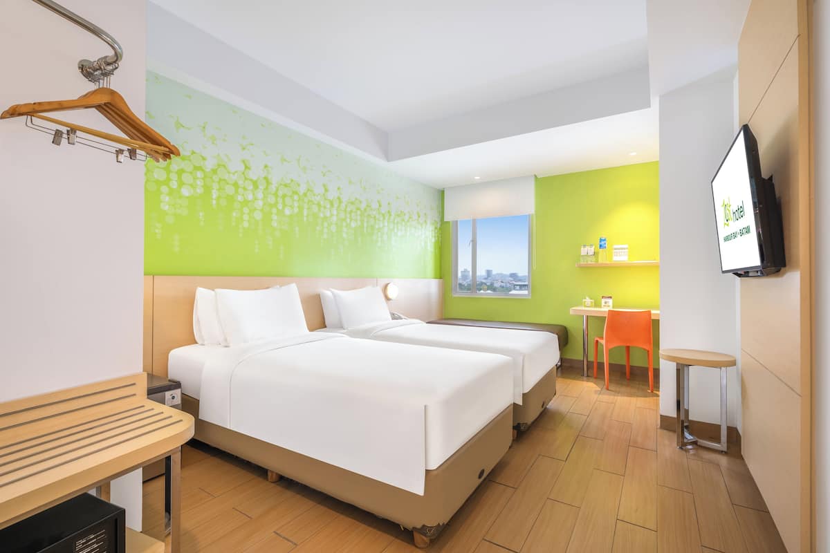 Ein Hotelzimmer mit zwei Betten, einem Holztisch, einem Fernseher und Blick auf die Stadt.