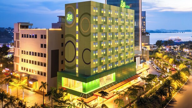 Un hotel de diseño moderno, con un llamativo letrero de 'Zest Hotel', varios pisos y vistas de la ciudad circundante y el agua.
