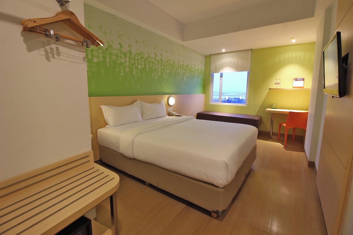 A hotel room with a bed, bedside table, a desk, and a chair.