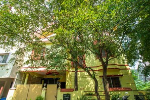 A yellow building with a red roof, a tree in front, and a sign with the number 510. - OYO 894 Apartment Hotel 510 Chetana (Bengaluru)